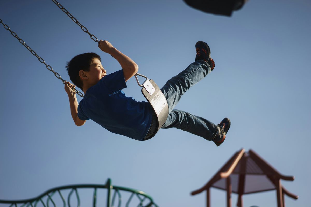 Boy swinging high on a playground swing under a blue sky