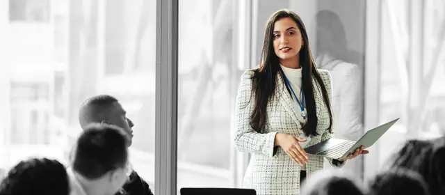Small business owner holding a laptop while leading a meeting with her team