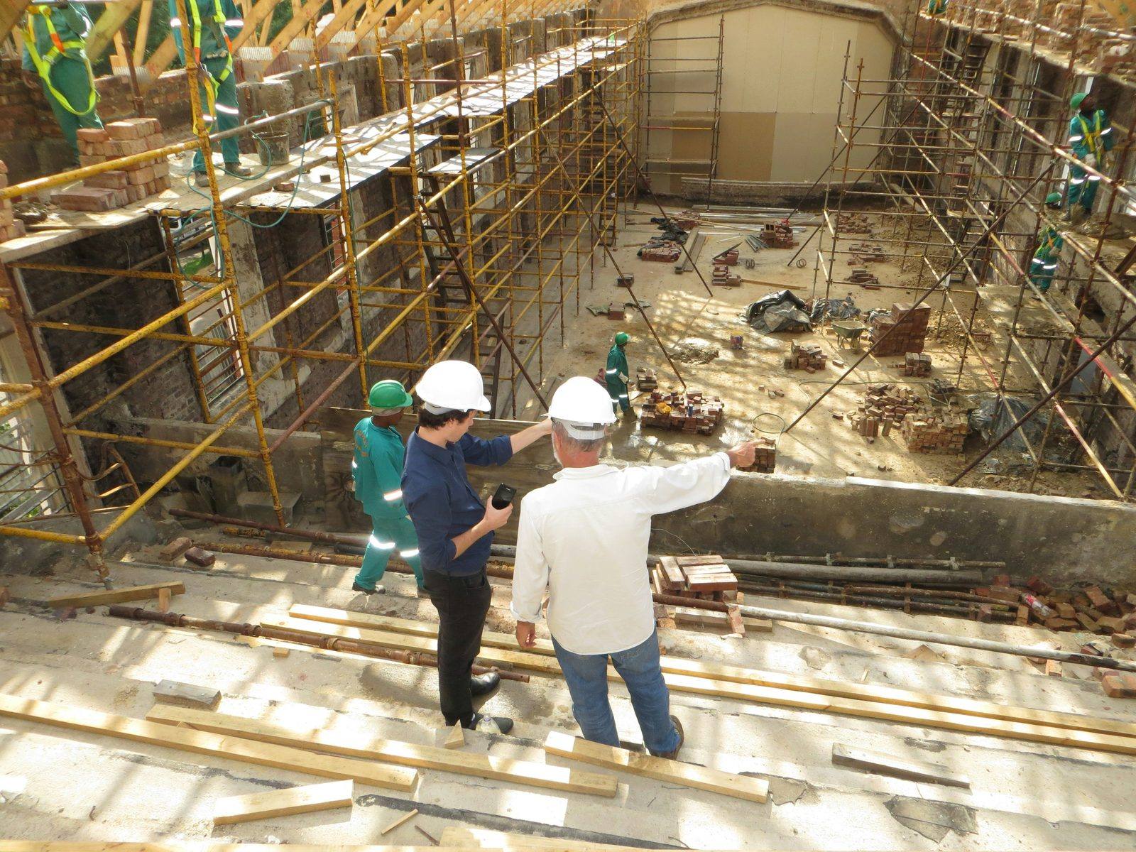 Construction site supervisors reviewing a build with crew on scaffolding, representing group health insurance for construction companies