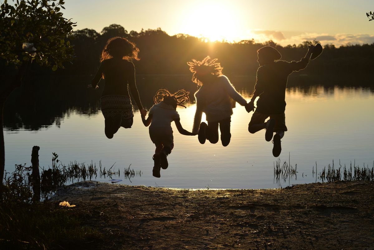 Family holding hands and jumping by a lake at sunset