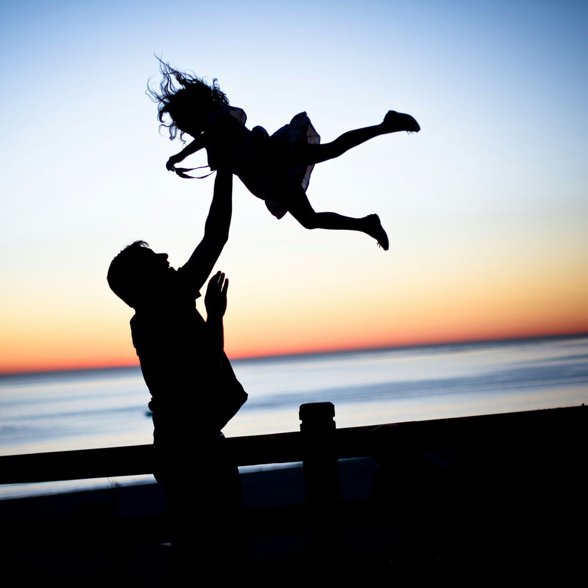 Parent lifting child at sunset - family health insurance coverage