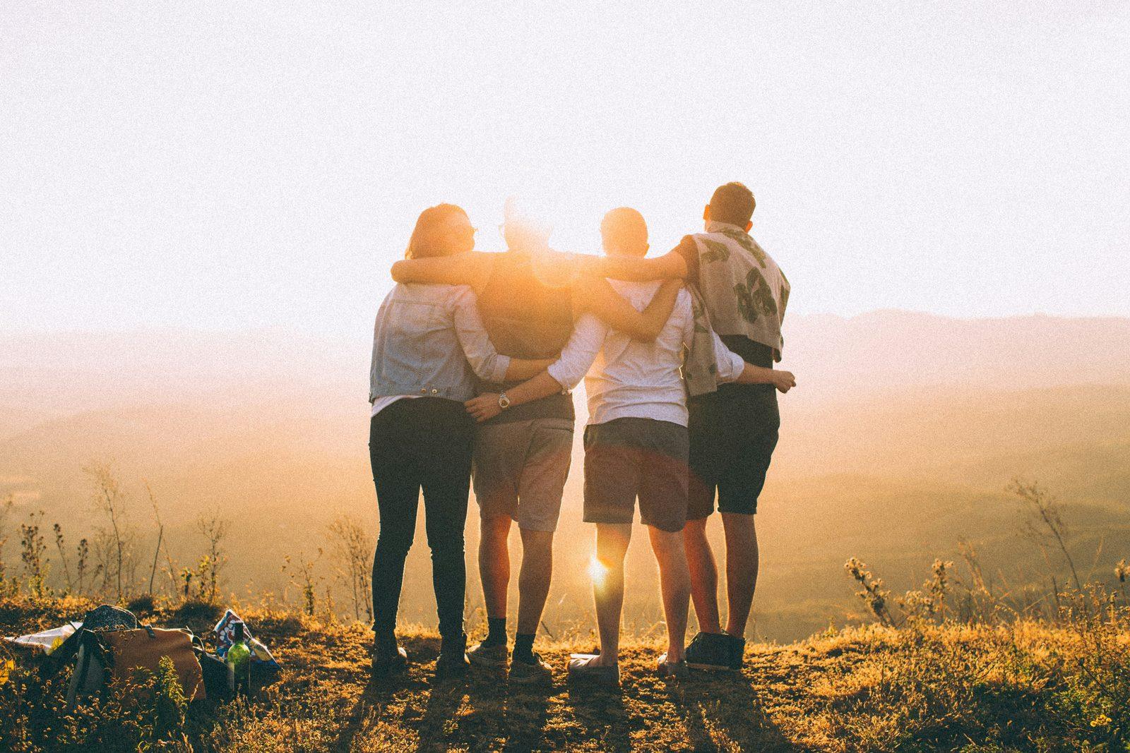 Four friends arm in arm watching the sunset, representing referring people you know for health coverage