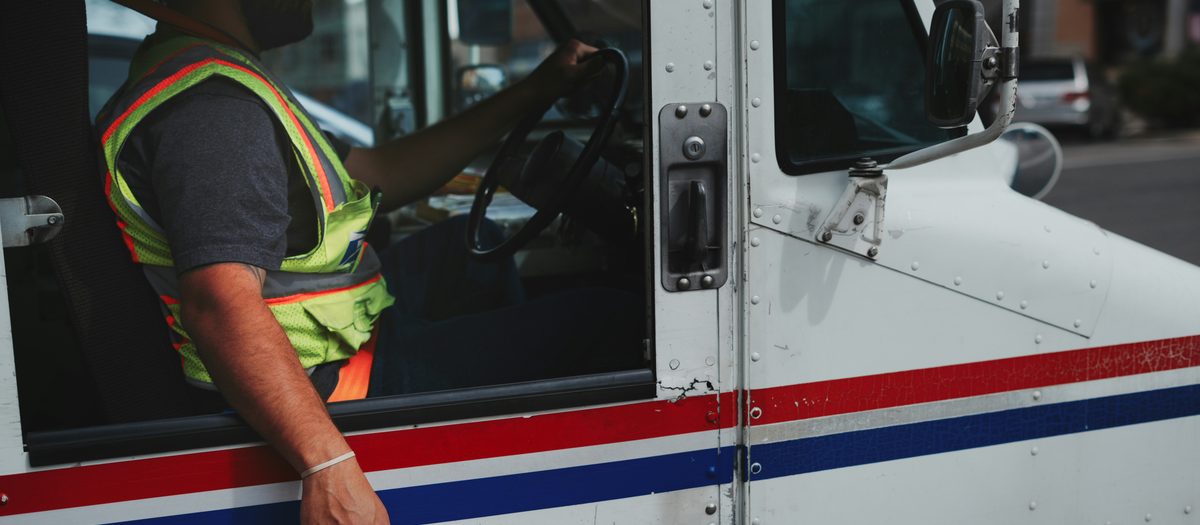 Mail delivery driver in a postal truck, illustrating mail-order pharmacy delivery for truck drivers on the road