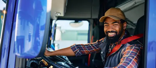 New CDL truck driver smiling from the window of a blue semi truck