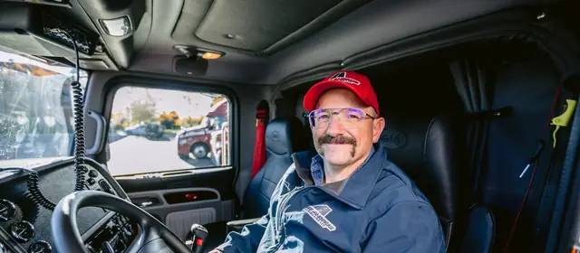 Owner-operator truck driver smiling in the driver's seat of his semi