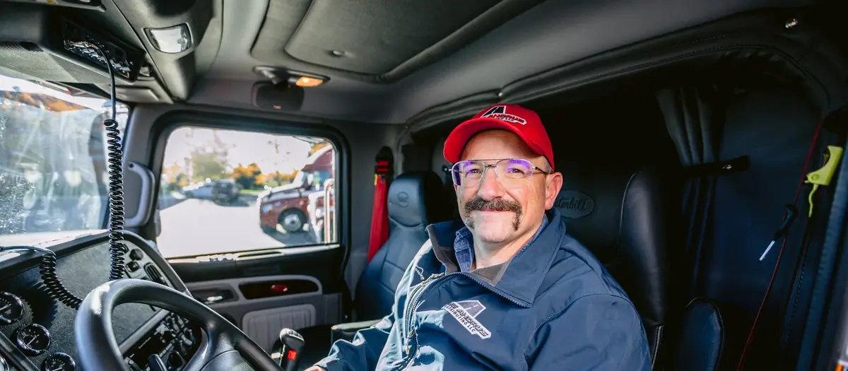 Owner-operator truck driver smiling in the driver's seat of his semi