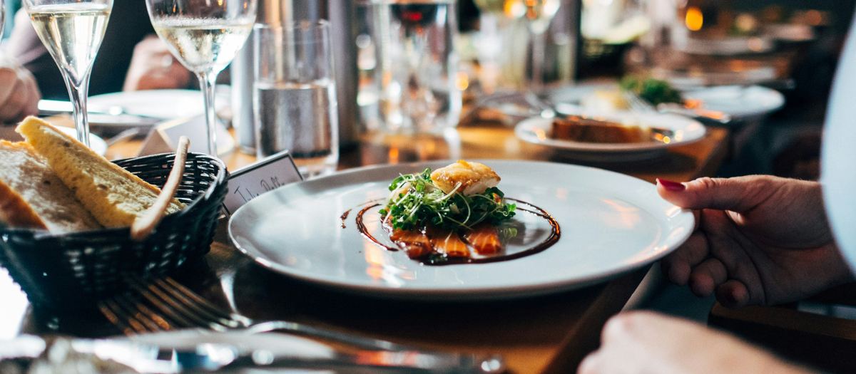 Restaurant server delivering a plated dish, a small business weighing ICHRA vs group health