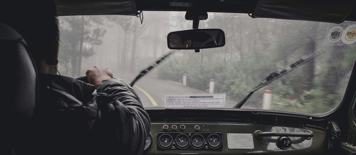 Driver at the wheel of a truck in fog and rain on a mountain road, illustrating the risk of needing medical care far from home