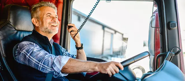 Team truck driver laughing on the CB radio in the cab of a semi truck