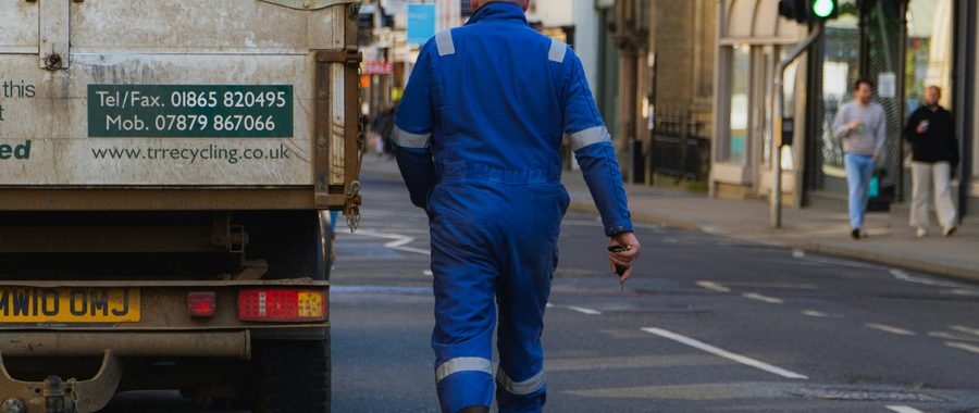 Driver in work coveralls walking along a street away from a parked truck, looking for care in an unfamiliar town