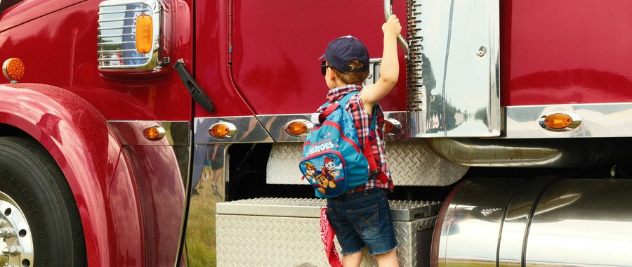 Child in cowboy boots climbing the step of a red semi truck, illustrating family health coverage for trucking households